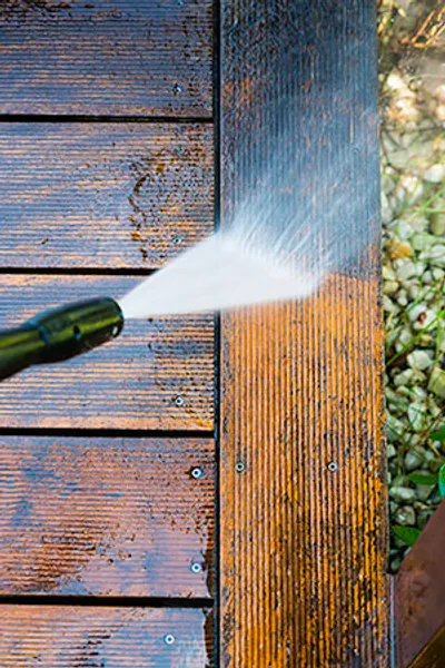 A person using a water hose to clean the wooden deck.