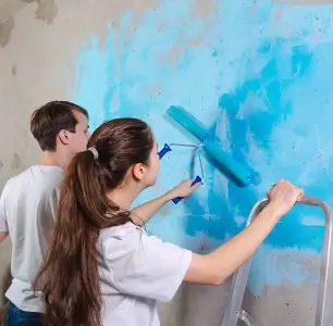 Two people painting a wall in blue tones using rollers.