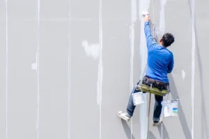 A person on a harness paints a wall white.