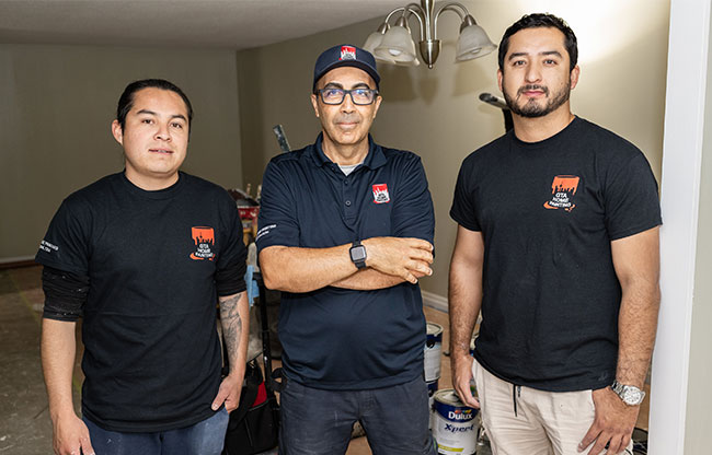 Three men wearing matching company t-shirts posing indoors.