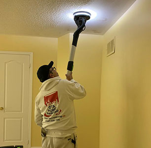 A person using an extension pole to paint a ceiling.