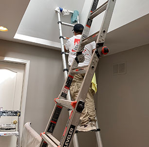 Person on a ladder painting a room.