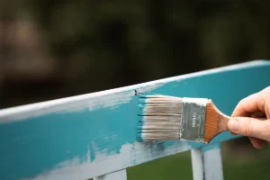 Applying teal paint to a wooden surface with a paintbrush.