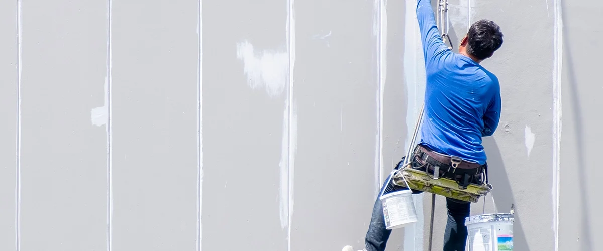 A person on a harness paints a wall white.